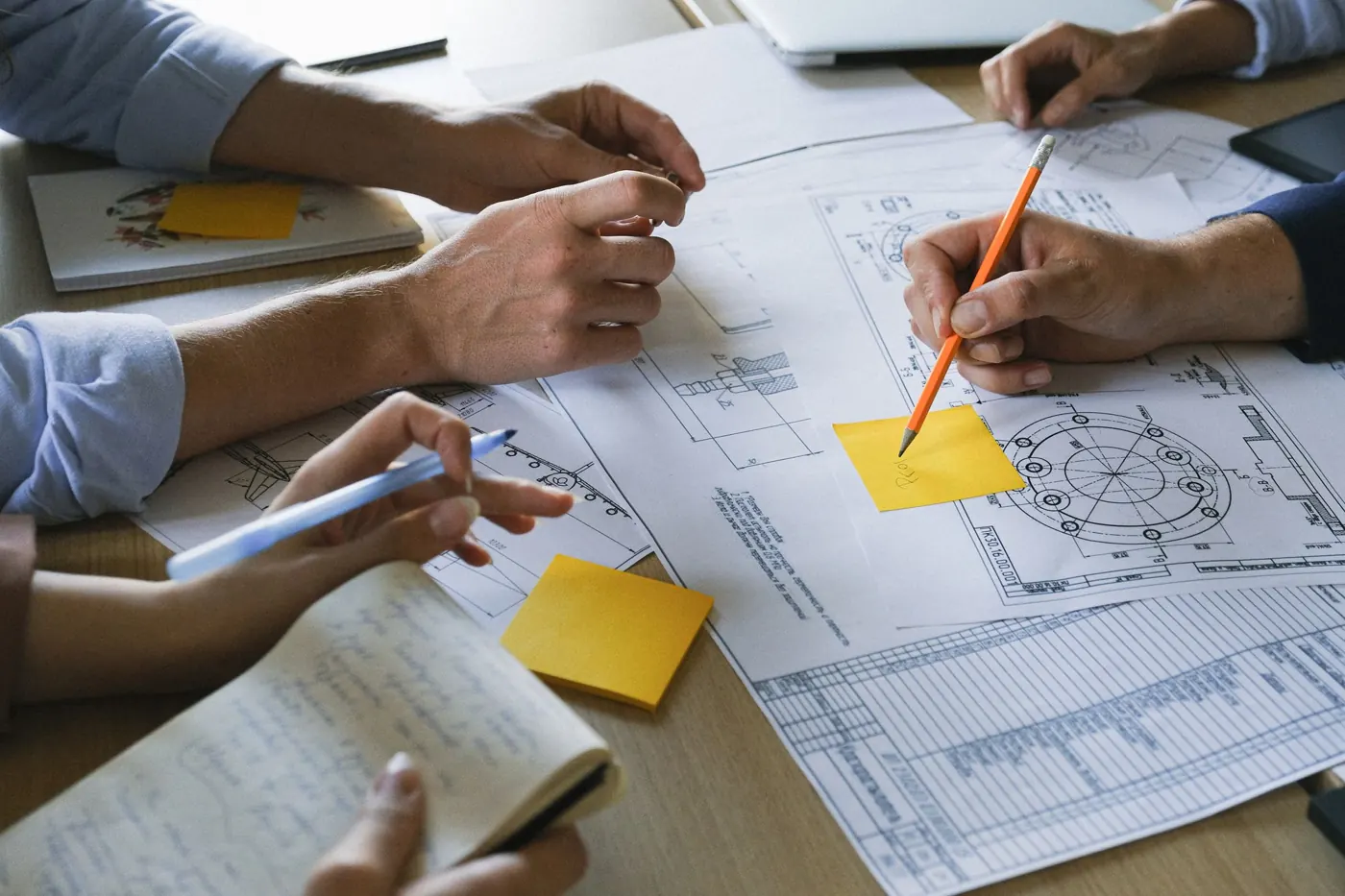 Mani al lavoro su disegni tecnici e appunti attorno a un tavolo di progetto